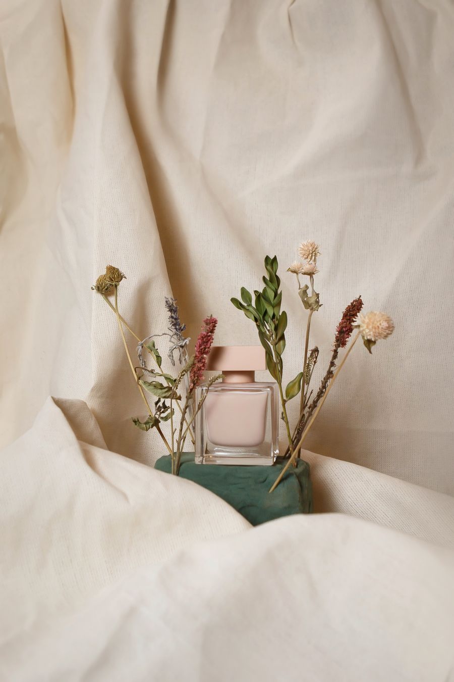 Perfume and dried flowers on ivory fabric